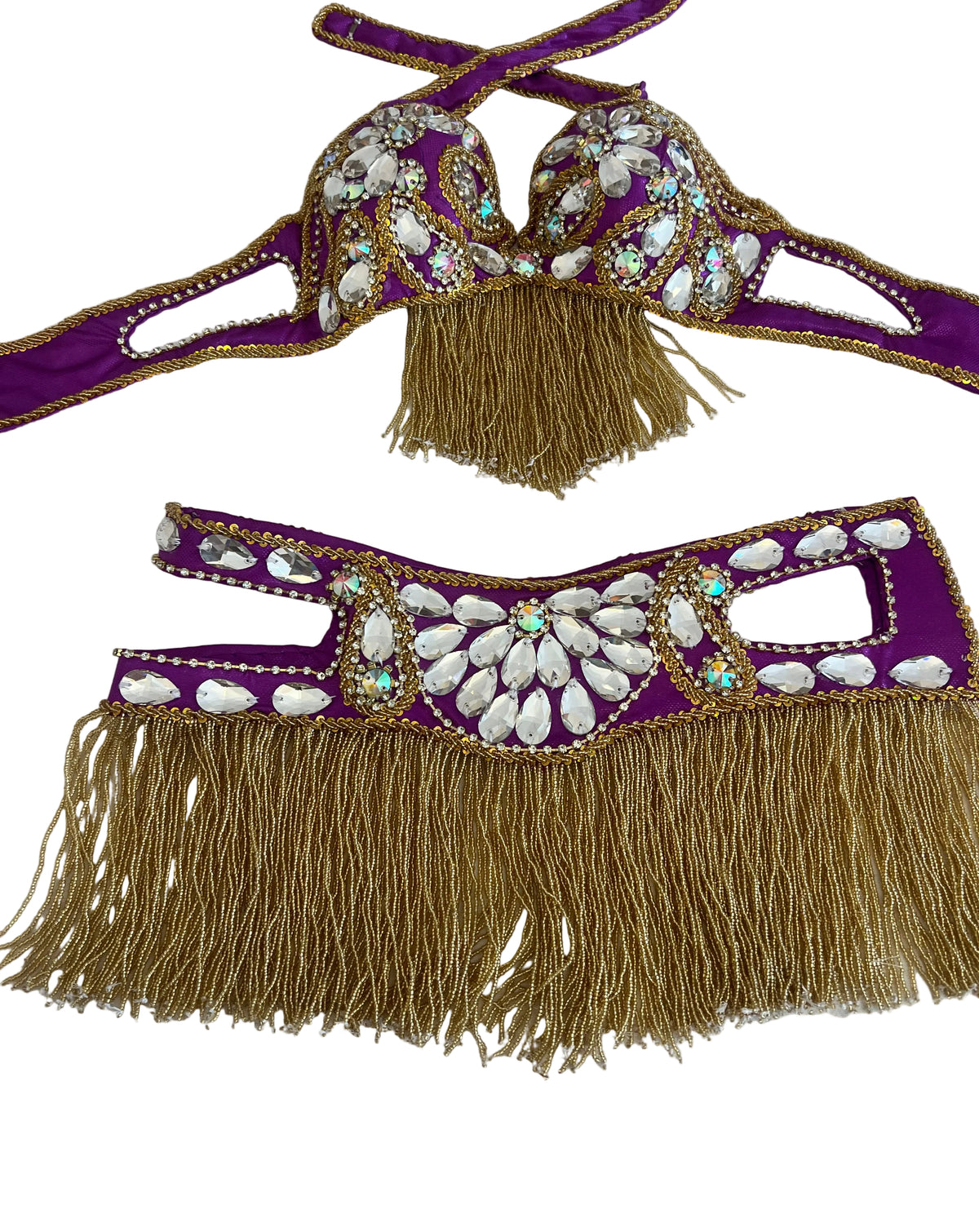 Purple belly dance costume set with gold fringe and white shell embellishments, laid flat on a white checkered surface.