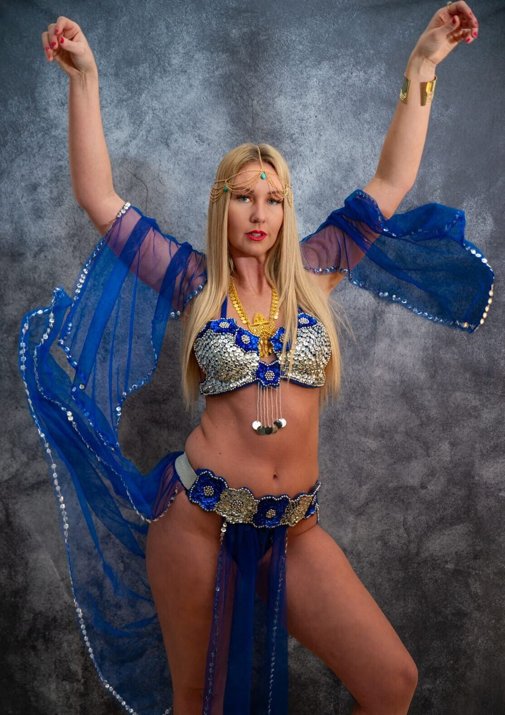 A woman posing in a royal blue belly dance costume with a braided hair accessory.
