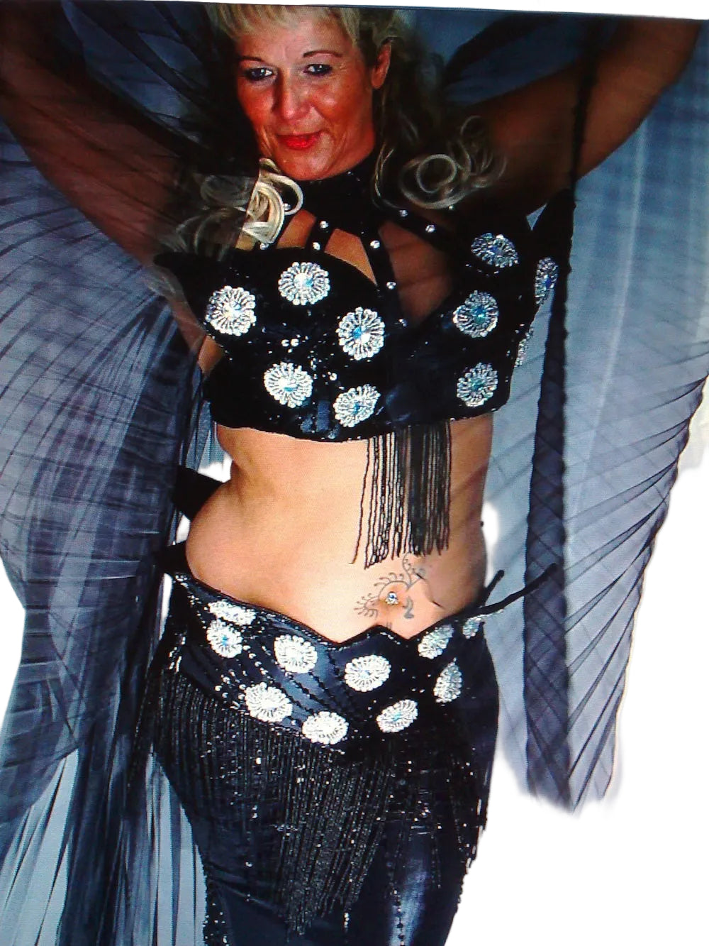A woman modeling a professional belly dance Outfit, which includes a skirt, belt, and top with bead and sequin decorations.